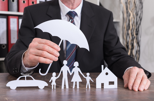 A man holding a paper cut out of an umbrella above paper dolls of a family 